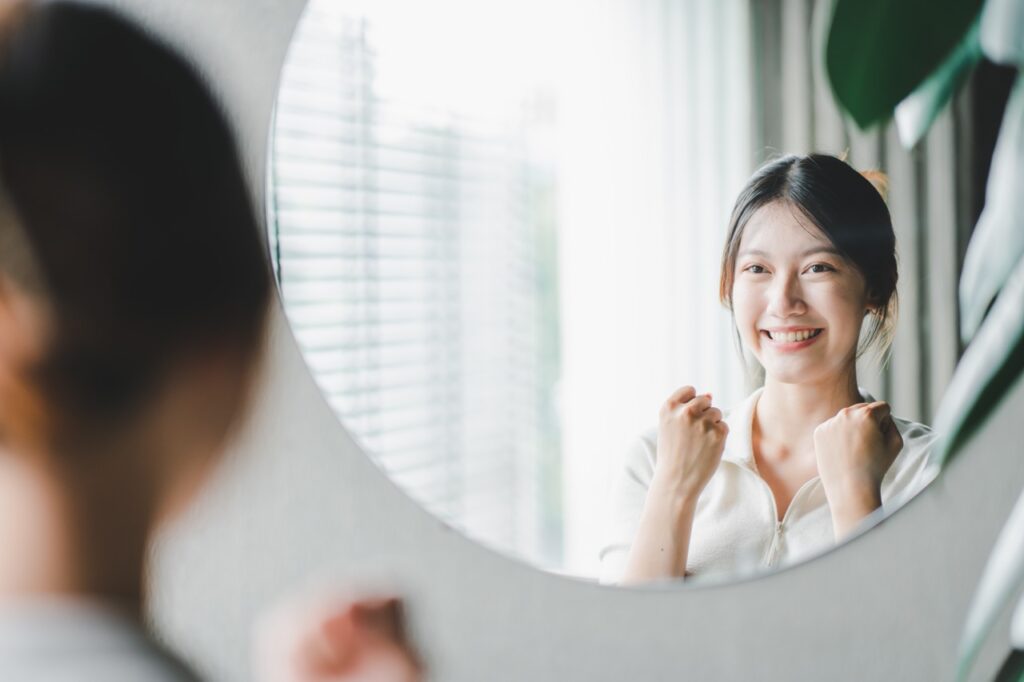 Woman looking in a mirror smiling because she has been receiving cbt therapy in fresno, california.